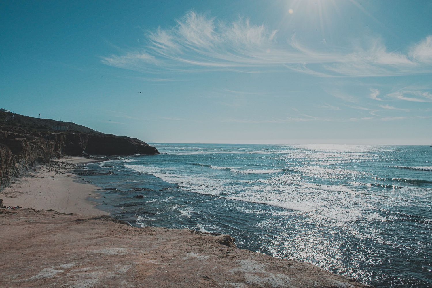 Scenic ocean view with waves breaking along a sandy coastline under turquoise sky.