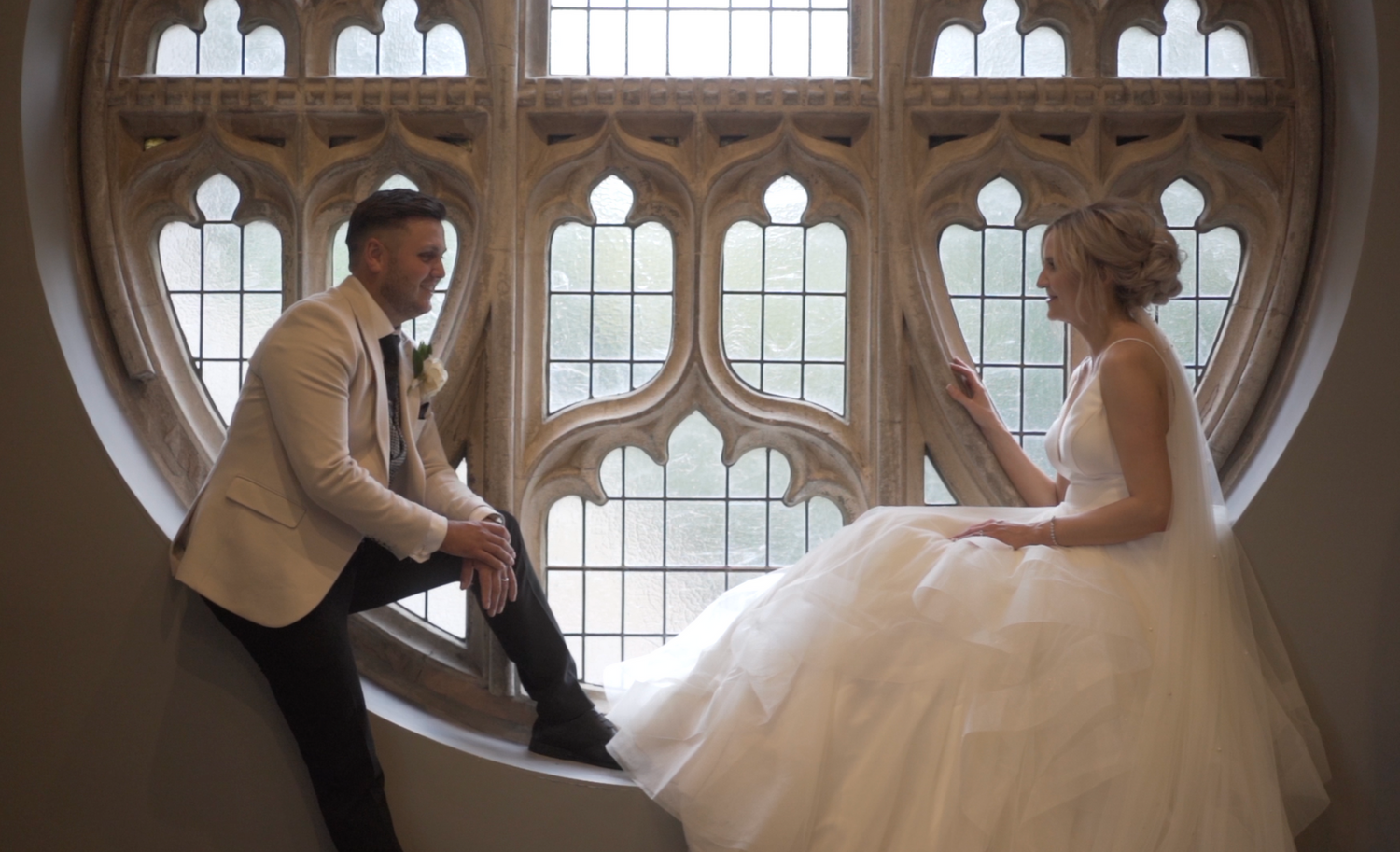 A couple poses playfully in an elegant arched window setting.