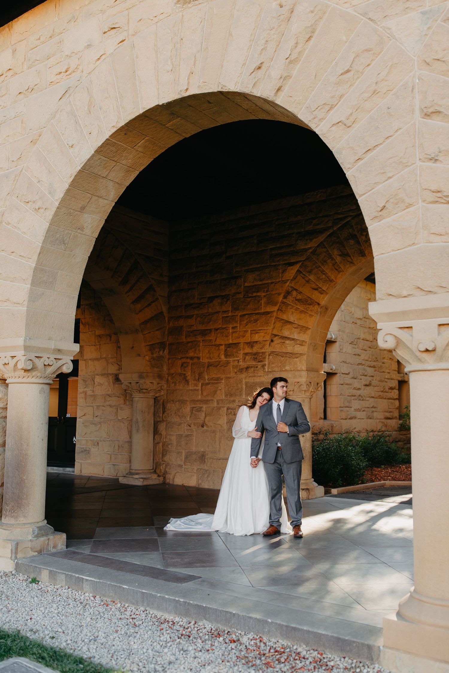 Couple shares tender moment under grand stone archway at historic venue.