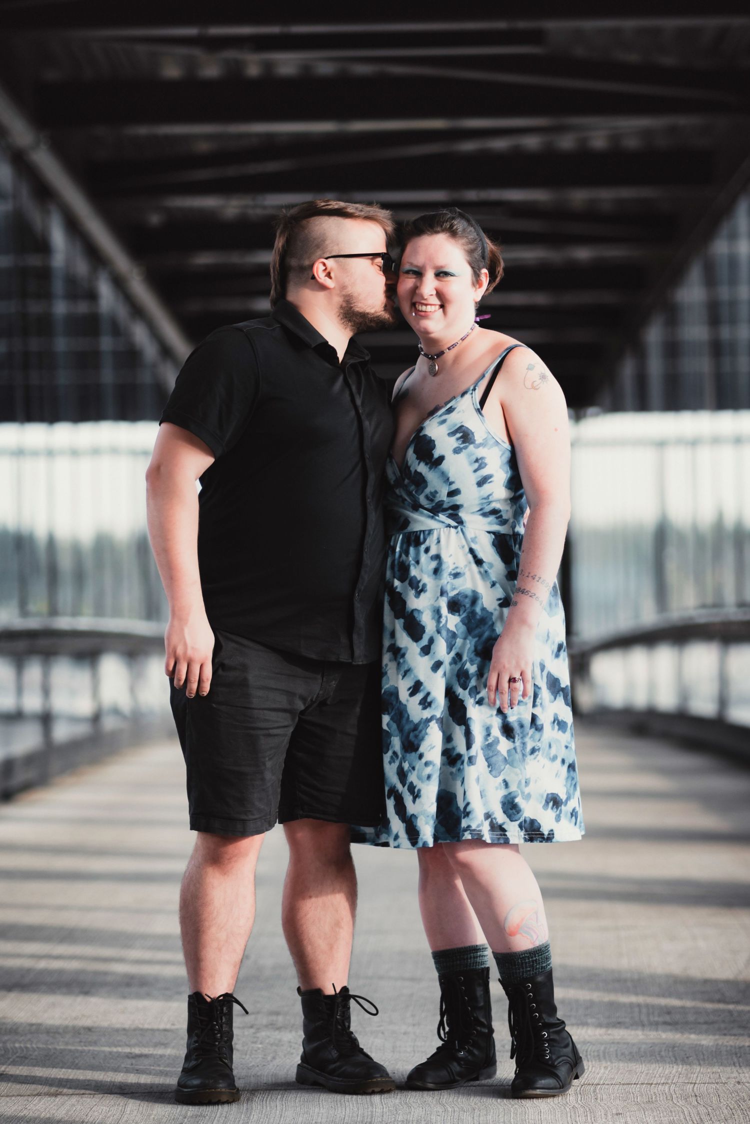 A romantic couple shares an intimate moment on a covered bridge wearing contrasting black and blue outfits.