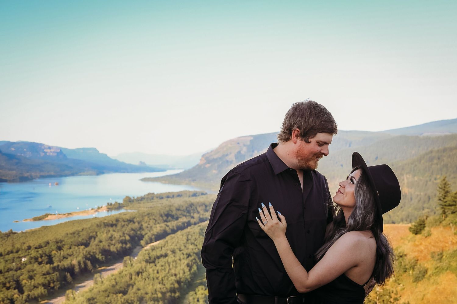 Couple embraces on mountaintop overlooking scenic lake and valley.