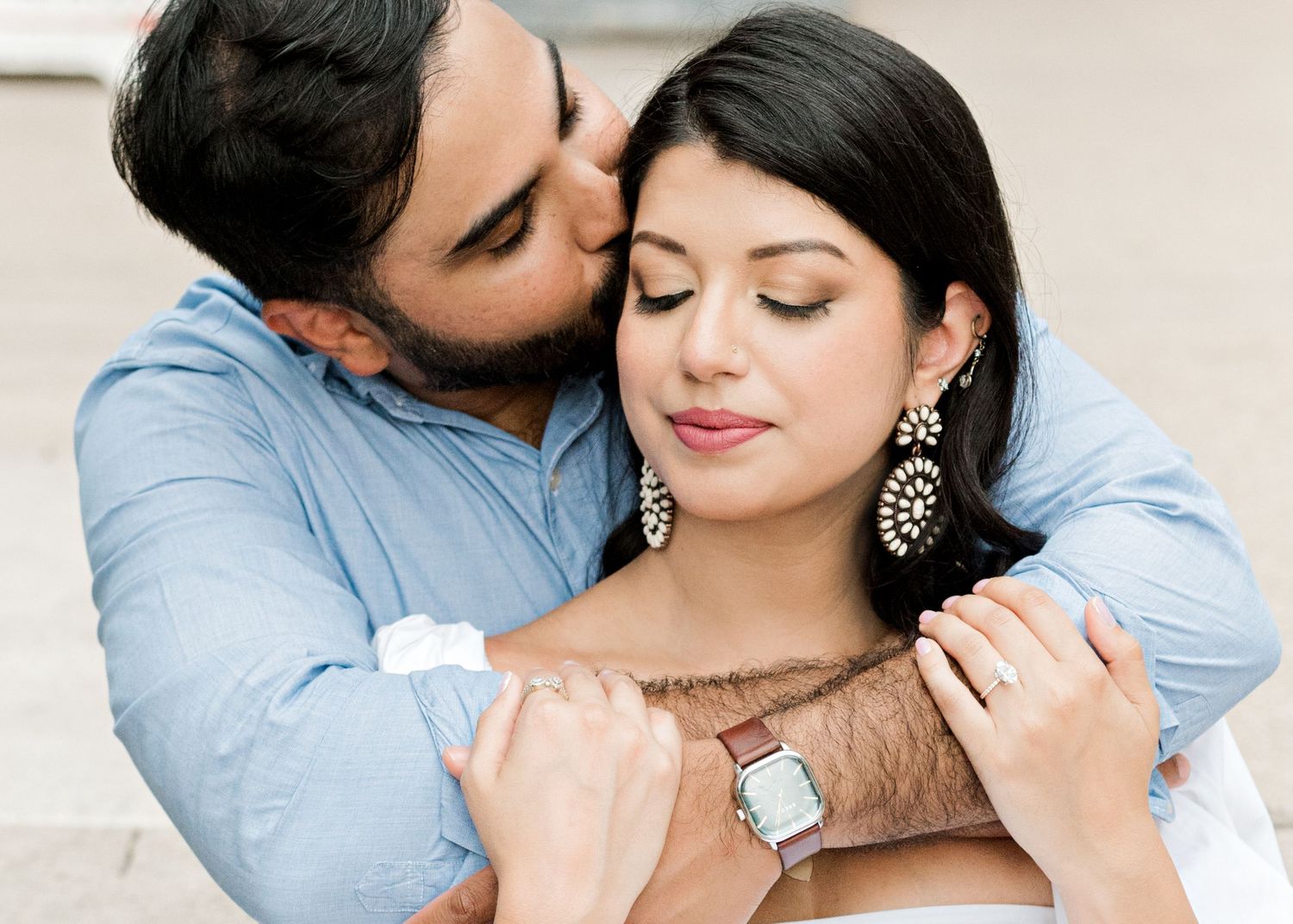 engaged couple in Austin, TX sitting together. guys arms wrapped around woman's shoulders as he kisses her cheek