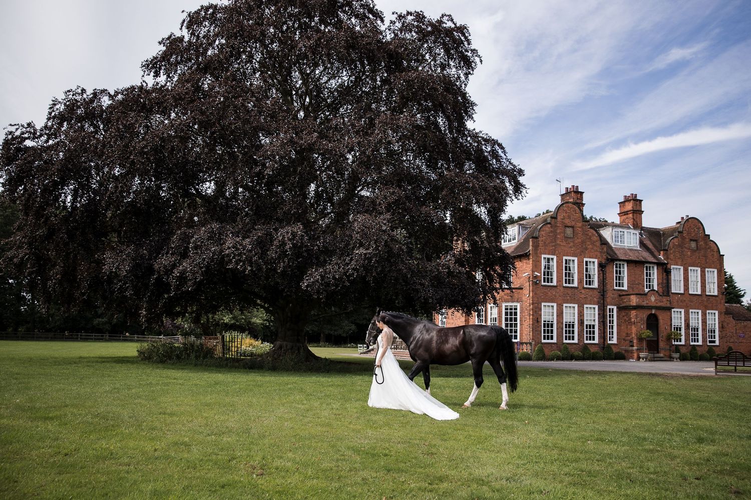Elegant red brick Georgian manor house surrounded by lush grounds and gardens on a sunny day.