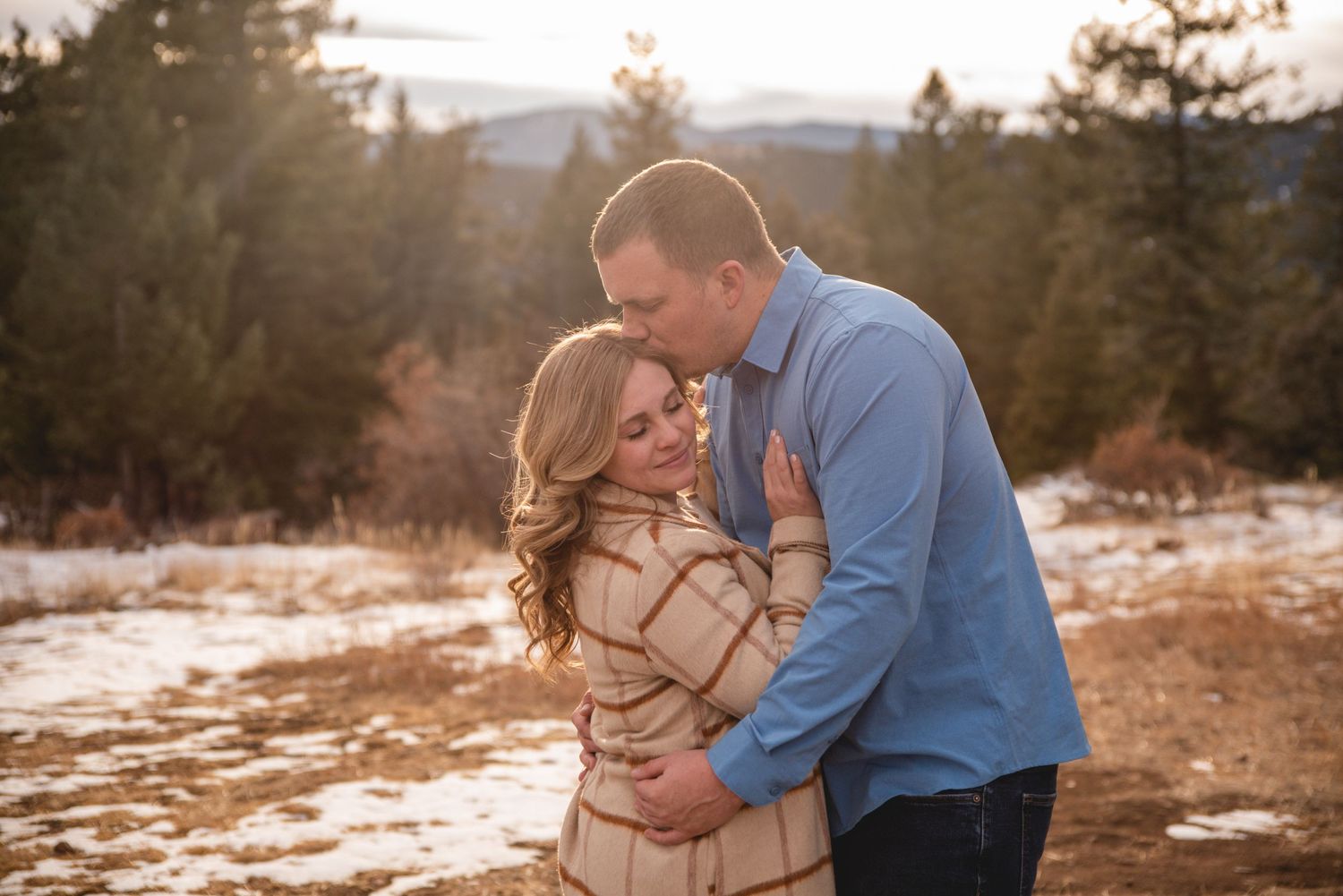 Intimate winter engagement portrait in snowy mountain landscape.