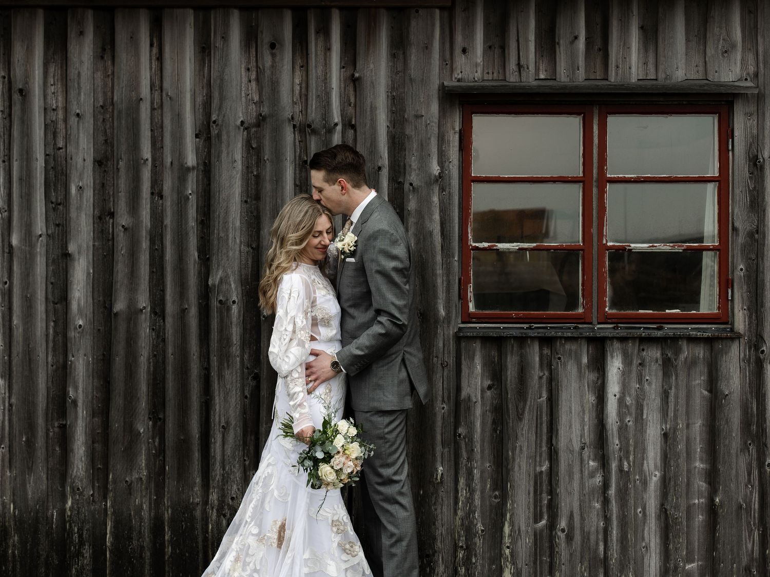 Newlyweds share an intimate moment against weathered wooden barn siding.