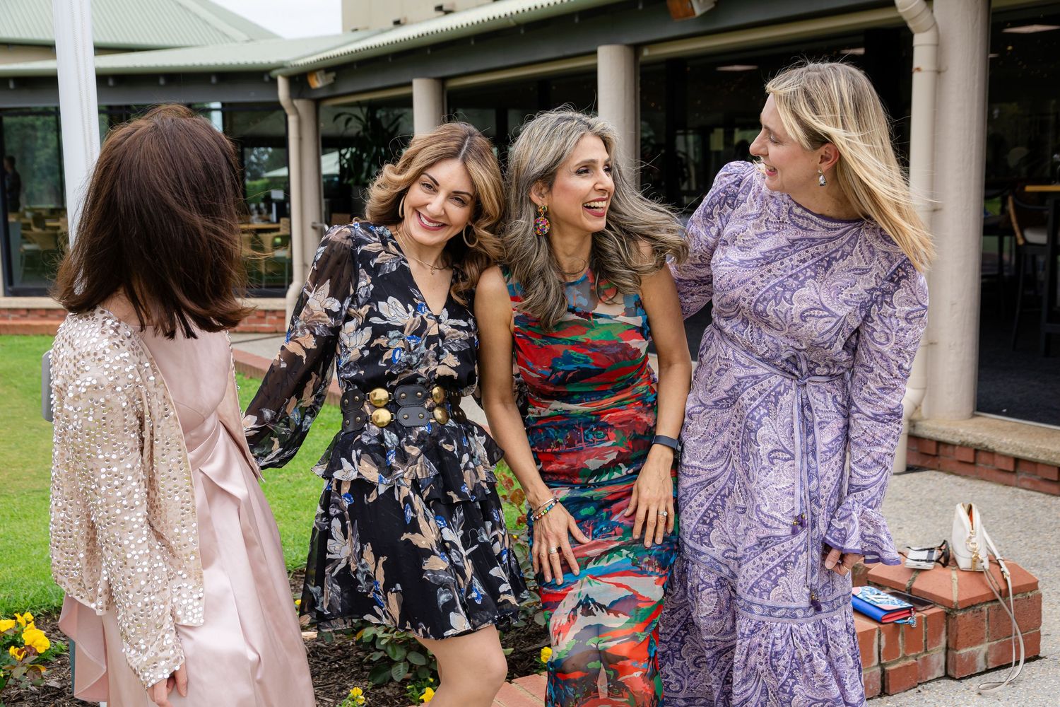 Group of women in floral dresses laughing together at outdoor gathering.
