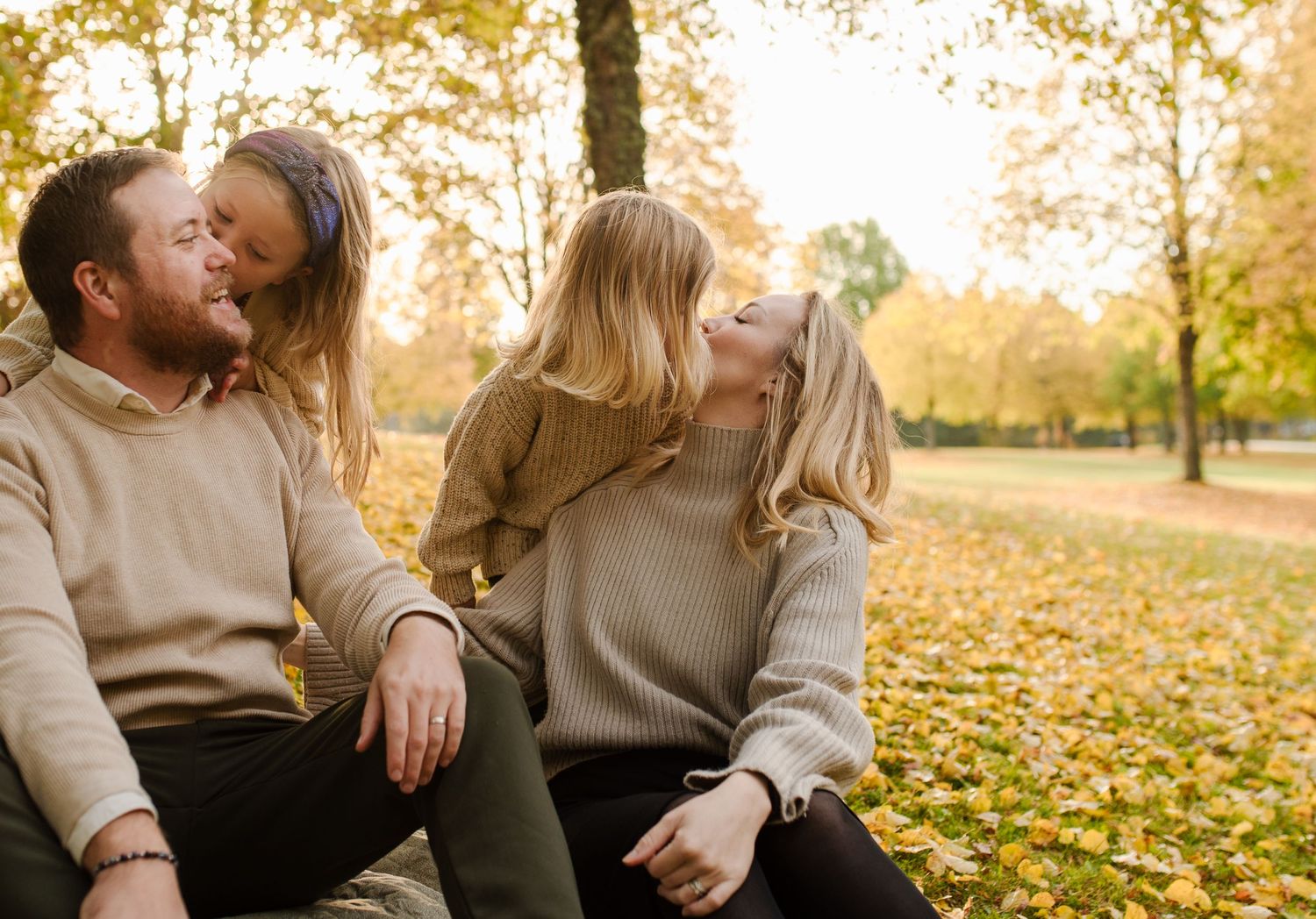 A tender family moment shared on fallen autumn leaves in a park setting.