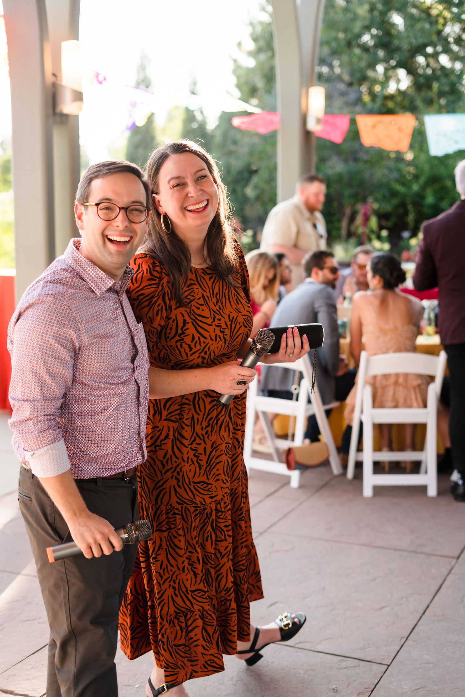 Couple shares a candid moment at outdoor party venue decorated with colorful banners.