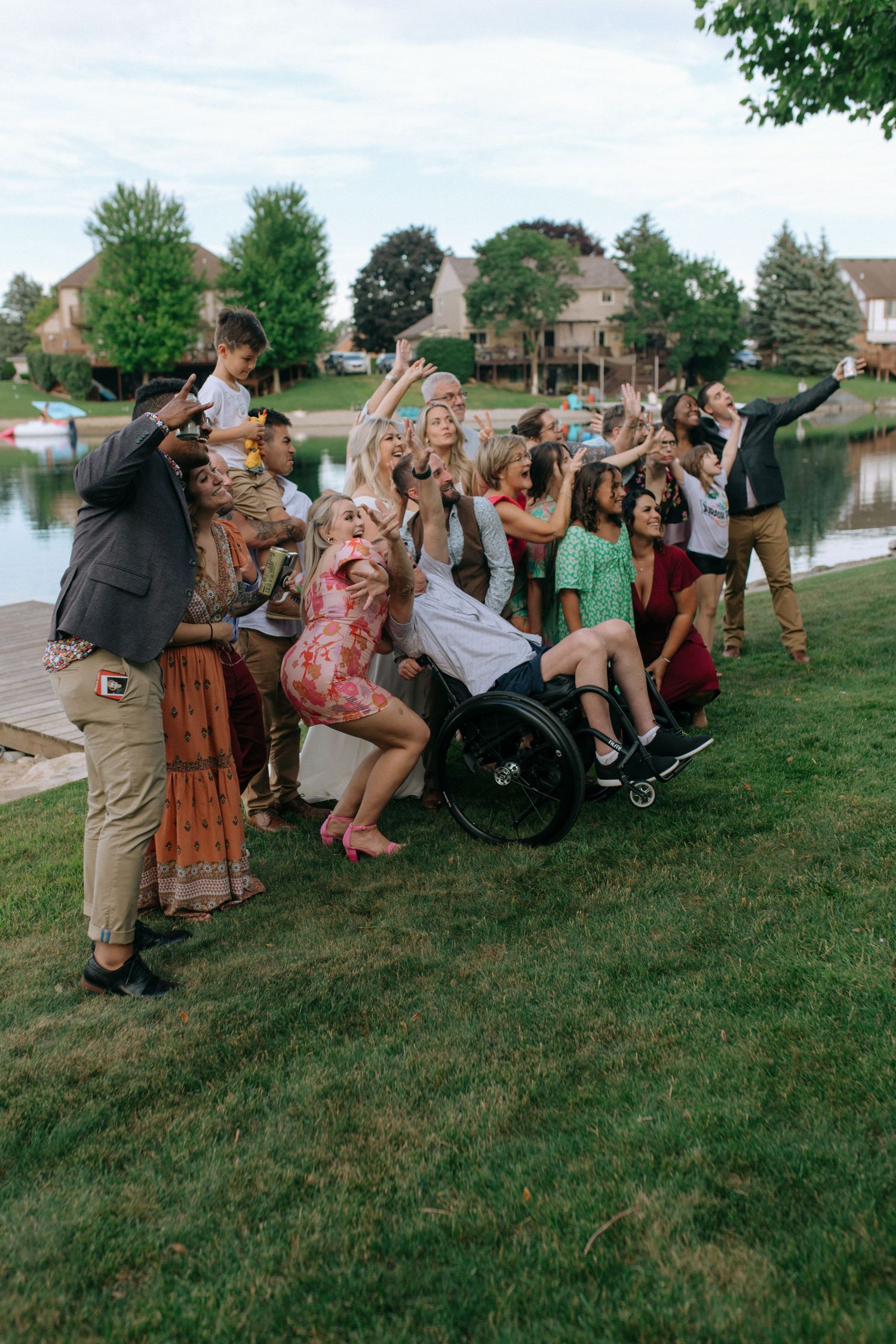 A joyful group poses together outdoors near a lake, celebrating with animated expressions.