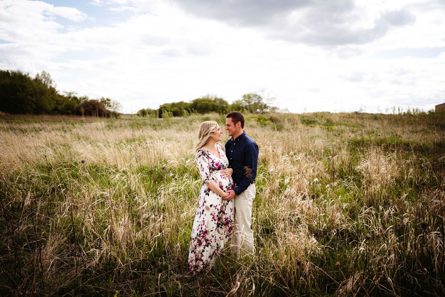 Romantic couple embracing in a field of tall grass during sunset.