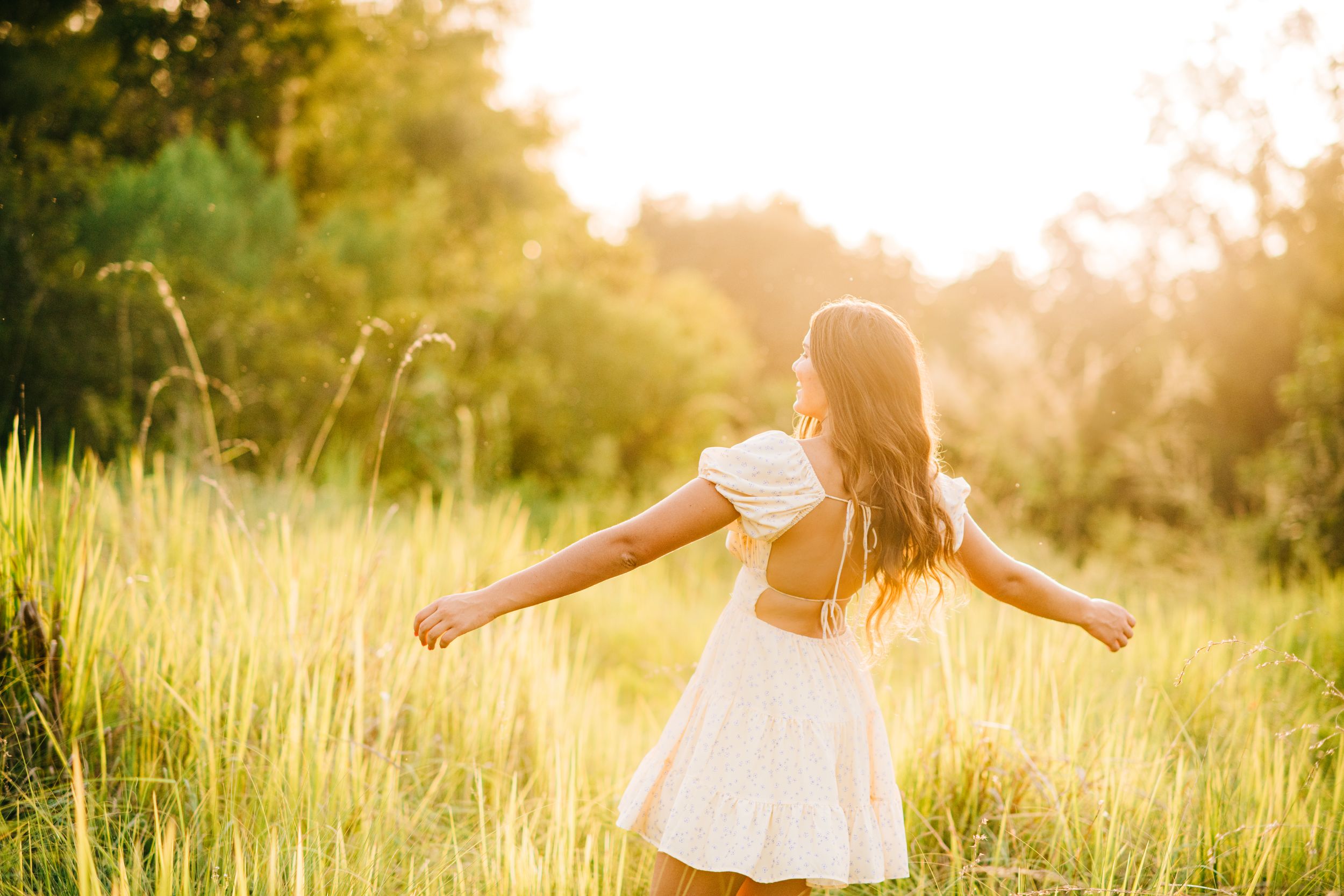 Figure in white dress spinning with arms outstretched in sunlit meadow.