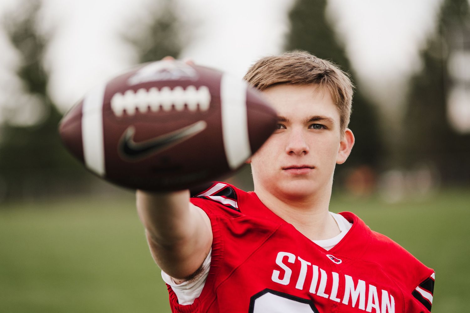 A football player in a red jersey practices catching drills on a grass field.