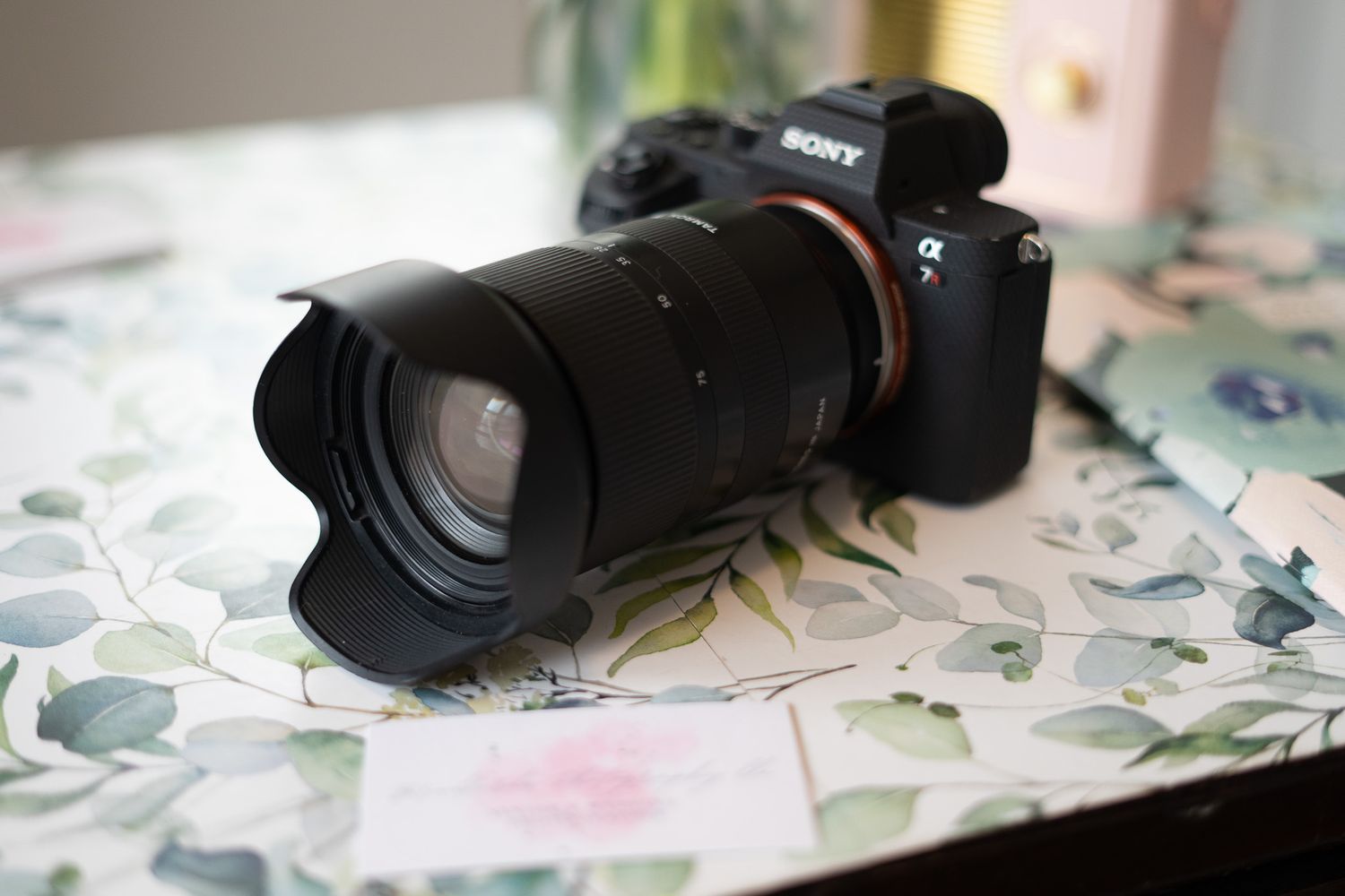 A Sony mirrorless camera with telephoto lens sits on a floral patterned surface.