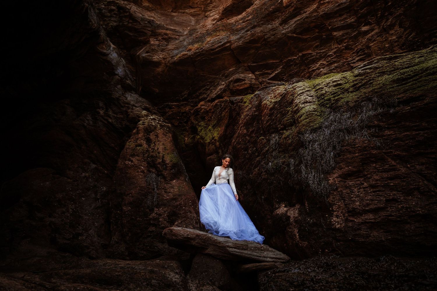 A bride in a purple tulle dress stands in a sea cave at Watermouth Cove