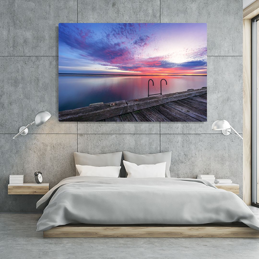 Modern bedroom interior with ocean sunset canvas prints mounted above concrete walls.