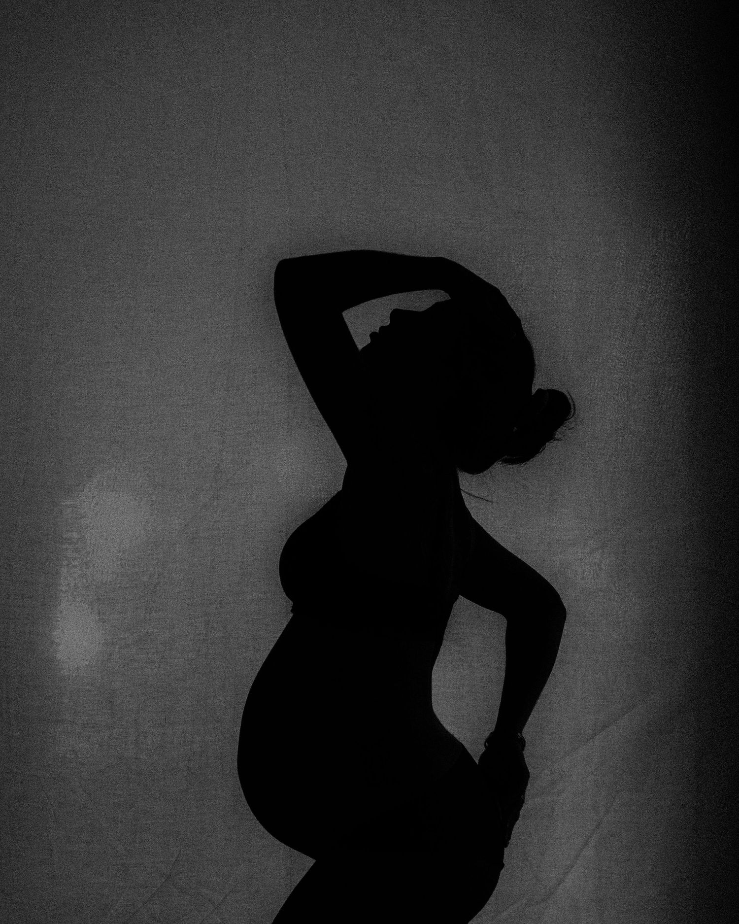 Artistic silhouette of a pregnant figure posing dramatically against a textured background.