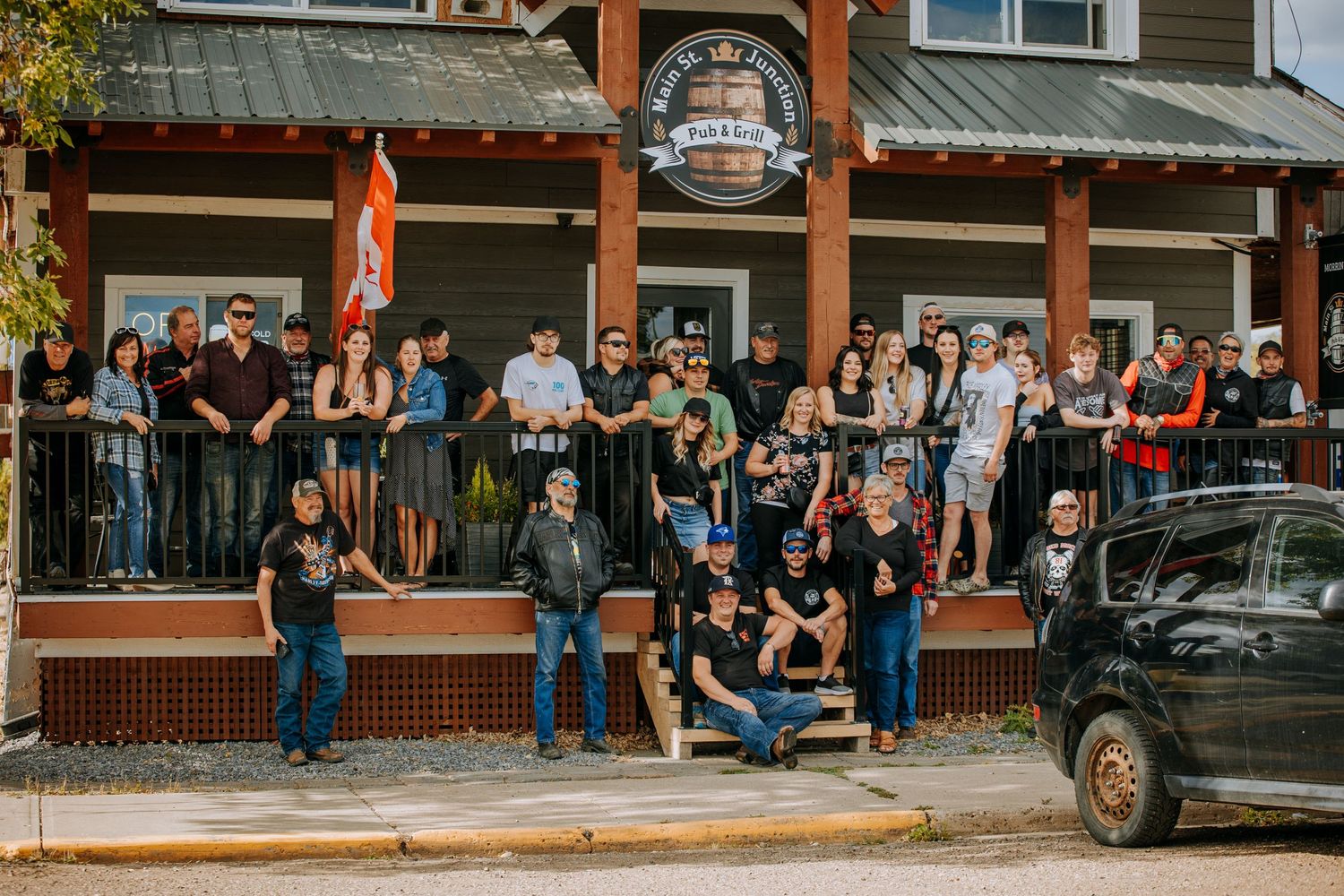 Crowd of people gathered on balcony of rustic wooden building watching street below.