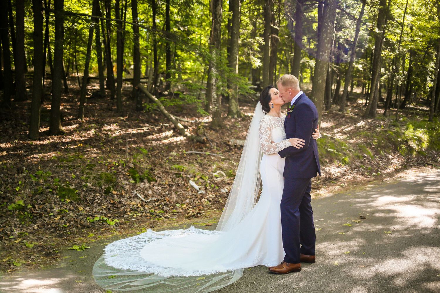 Bride with long veil kissing groom on forest path, Door County, Wisconsin destination wedding photography