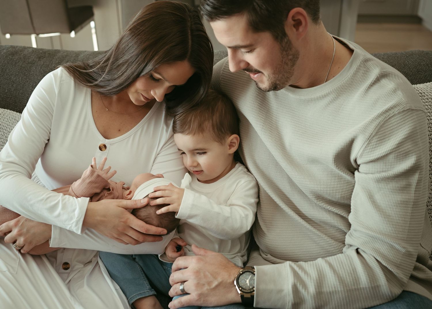Intimate family moment on grey couch showing tender interaction in casual home setting.