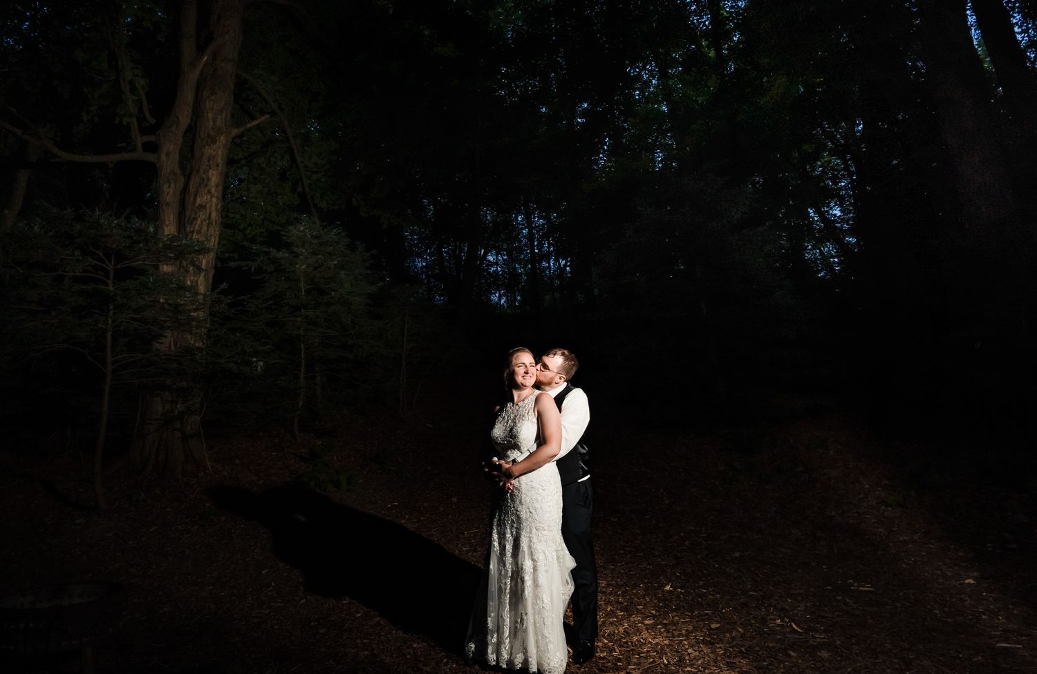 Wedding couple walking through a wooded path at dusk with romantic lighting.