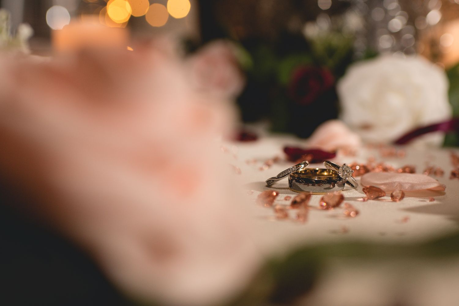 Close-up of wedding rings on pink surface with bokeh lights in background.