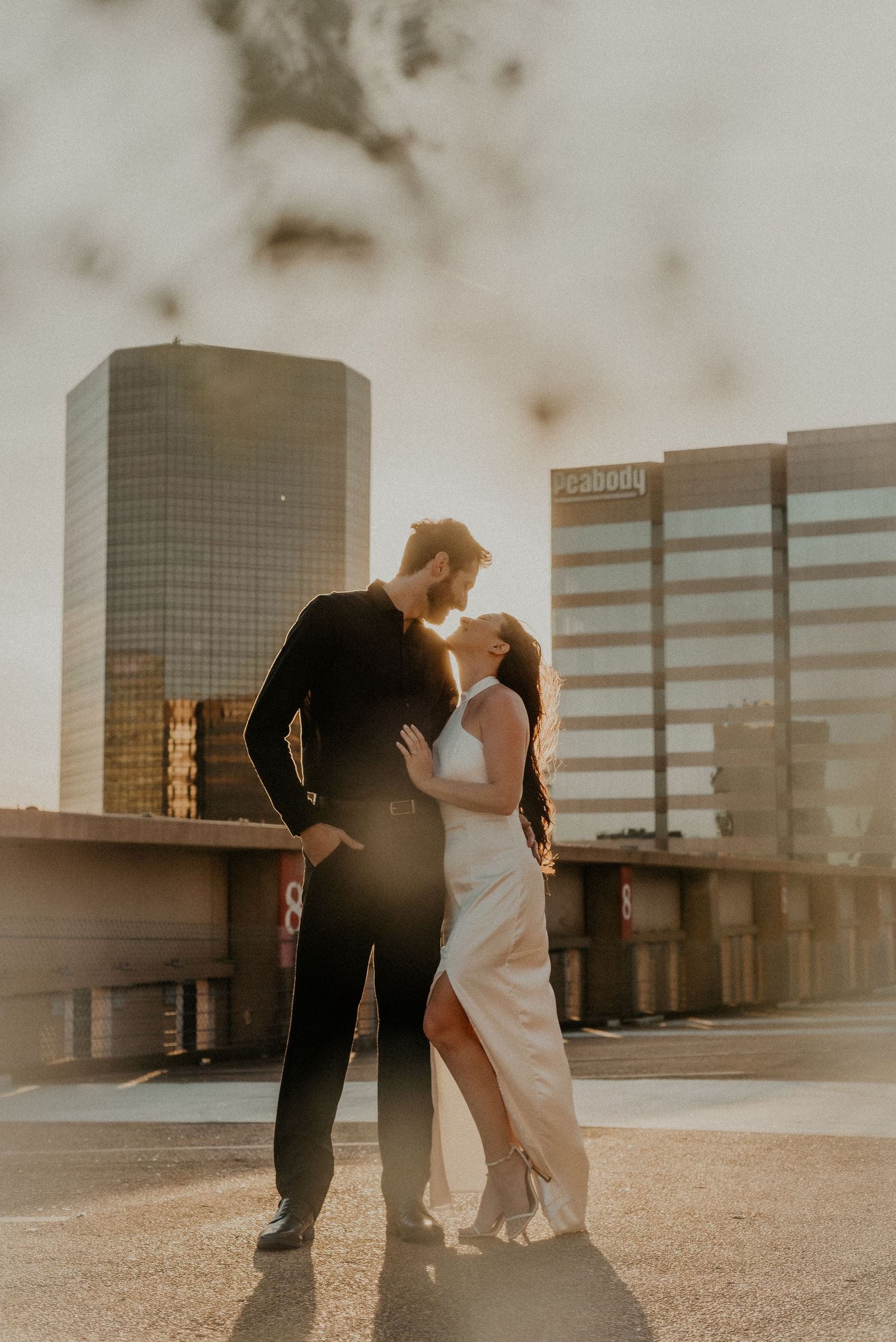 A romantic sunset portrait of a couple in formal wear against a city skyline.