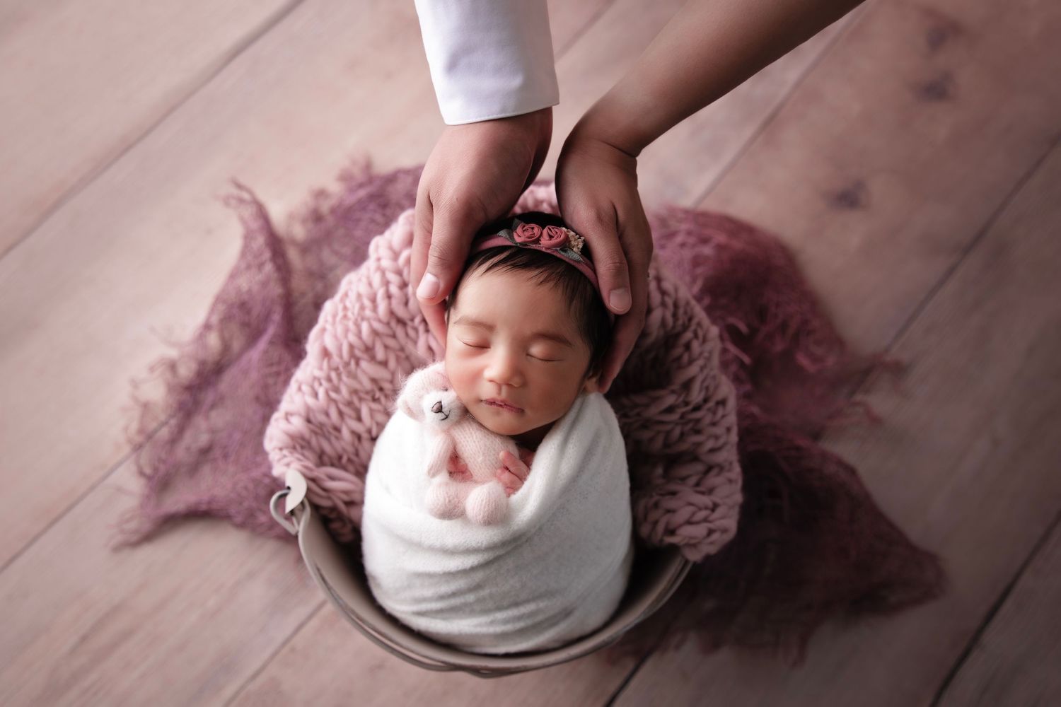 Newborn wrapped in white swaddle on pink knit blanket during professional photo session.