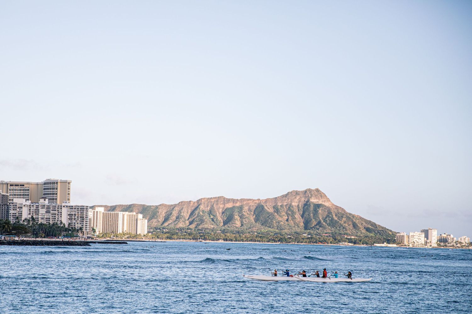 View of Diamond Head crater and Waikiki Beach with paddlers in the ocean on a sunny day in Hawaii.