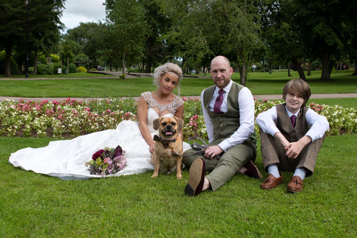 Wedding party relaxing on grass in a scenic garden setting.
