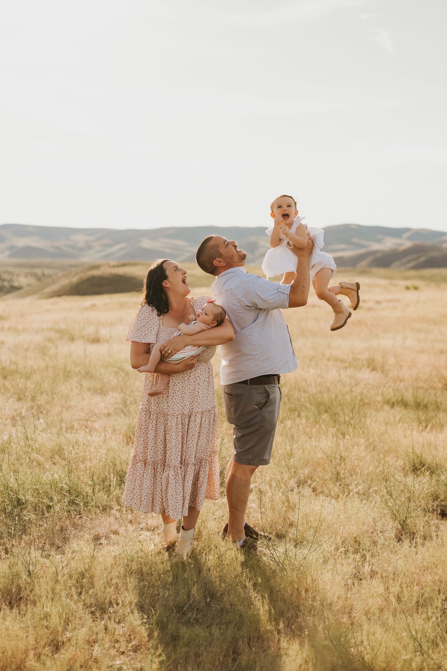 A family plays together in a sunny meadow with rolling hills in the background.