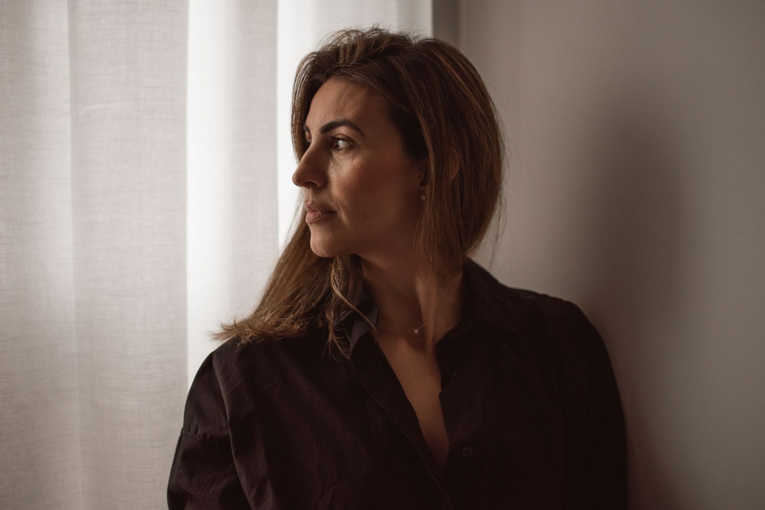 Contemplative portrait by window with soft natural lighting.