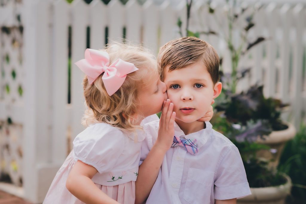 Blonde sister (2) kisses her older (4) in their Easter outfits in front of the Summerour House in Johns Creek, GA