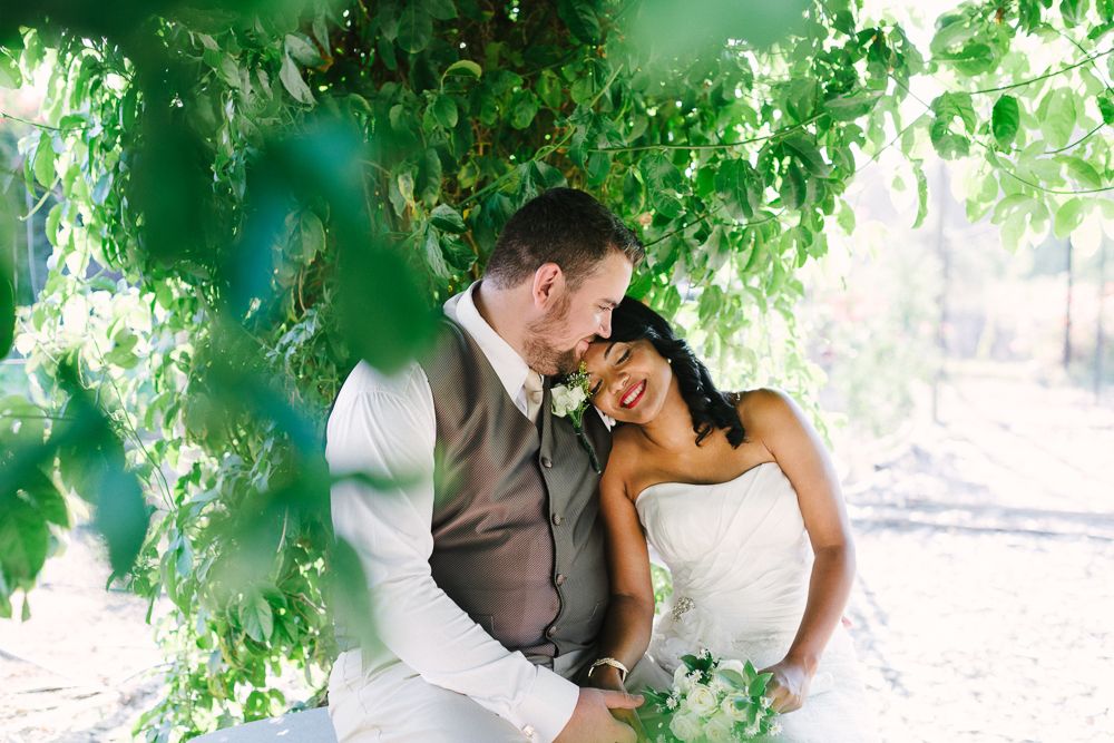 A romantic moment shared between newlyweds under lush green foliage.