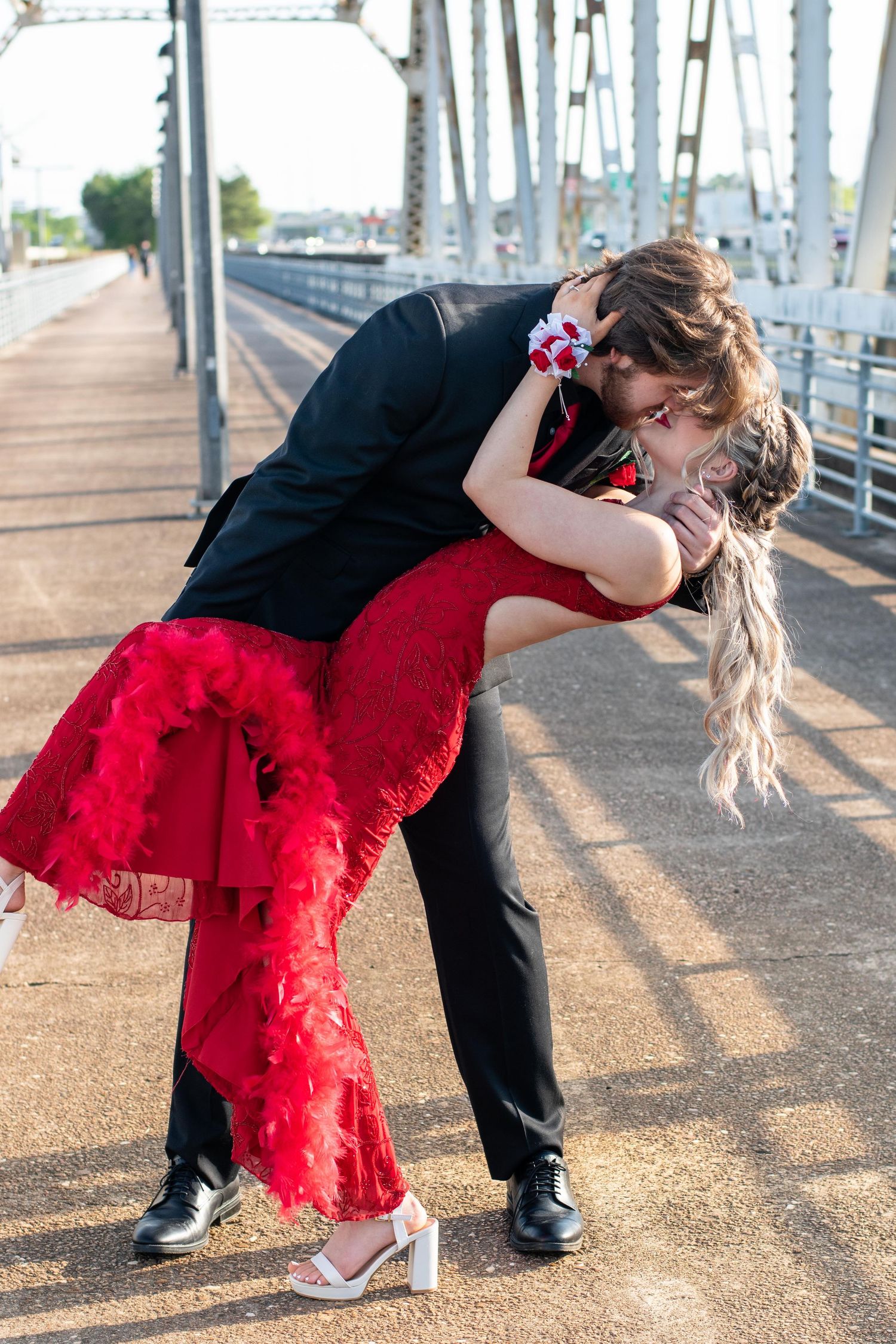 Romantic dip pose between couple on bridge with person in red dress and formal black attire.