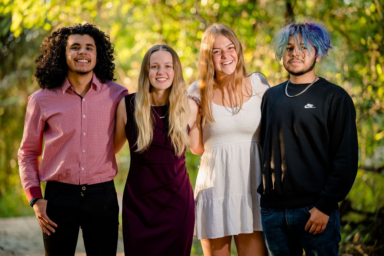 Four friends smile for a portrait outdoors with autumn foliage in the background.