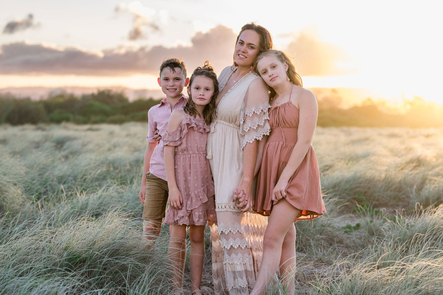 Family group portrait in coordinated pink outfits against sunset meadow backdrop.
