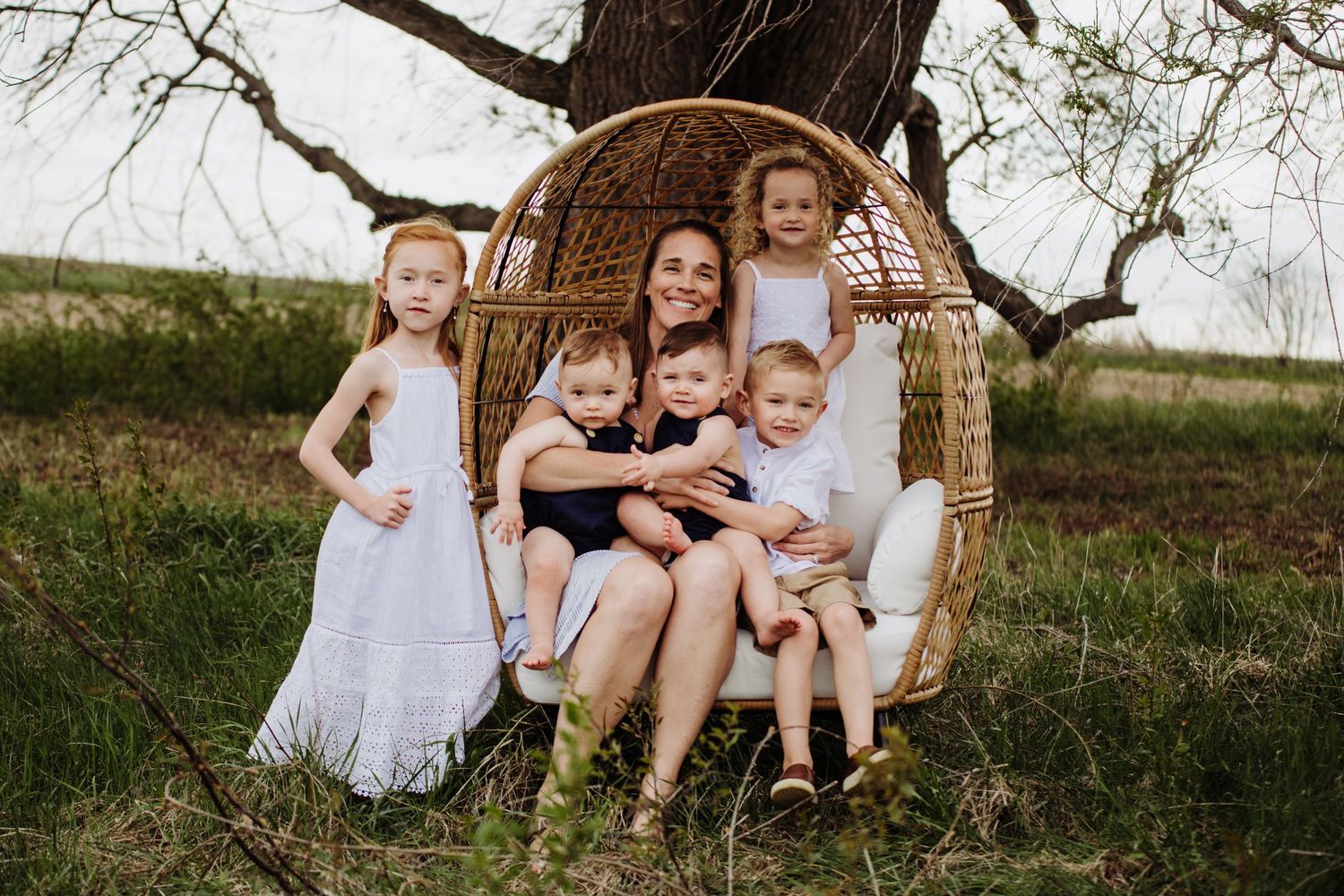 Family enjoying a relaxing moment together in a hanging rattan egg chair under a tree in a natural outdoor setting.
