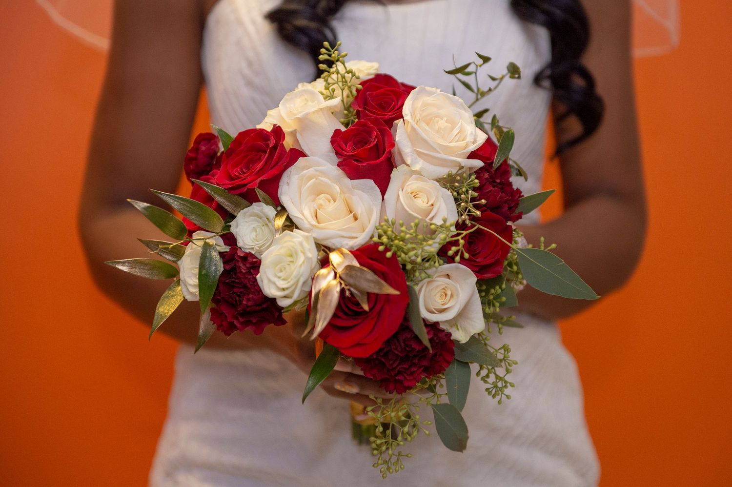 Classic bridal bouquet of red and white roses with eucalyptus against vibrant orange background.