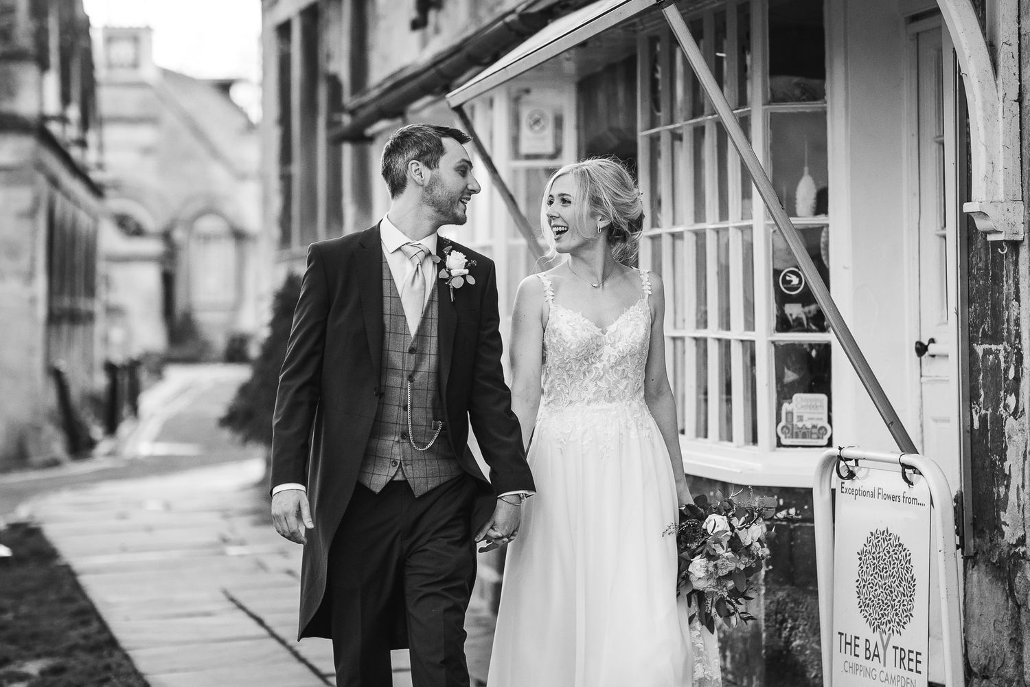 Black and white portrait of couple in wedding attire on historic cobblestone street.