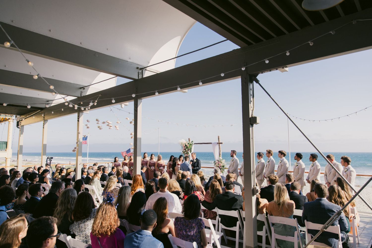 Large crowd gathered at an outdoor wedding venue overlooking the ocean.
