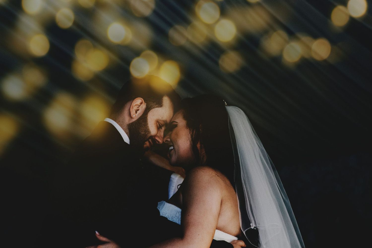 Romantic wedding couple embracing under twinkling lights at night.