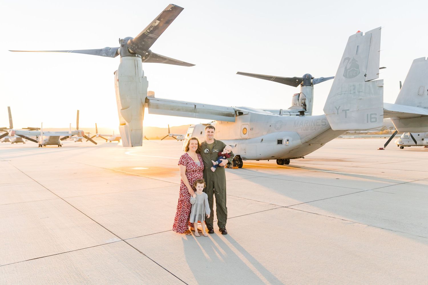 Military family poses in front of V-22 Osprey aircraft during golden hour.