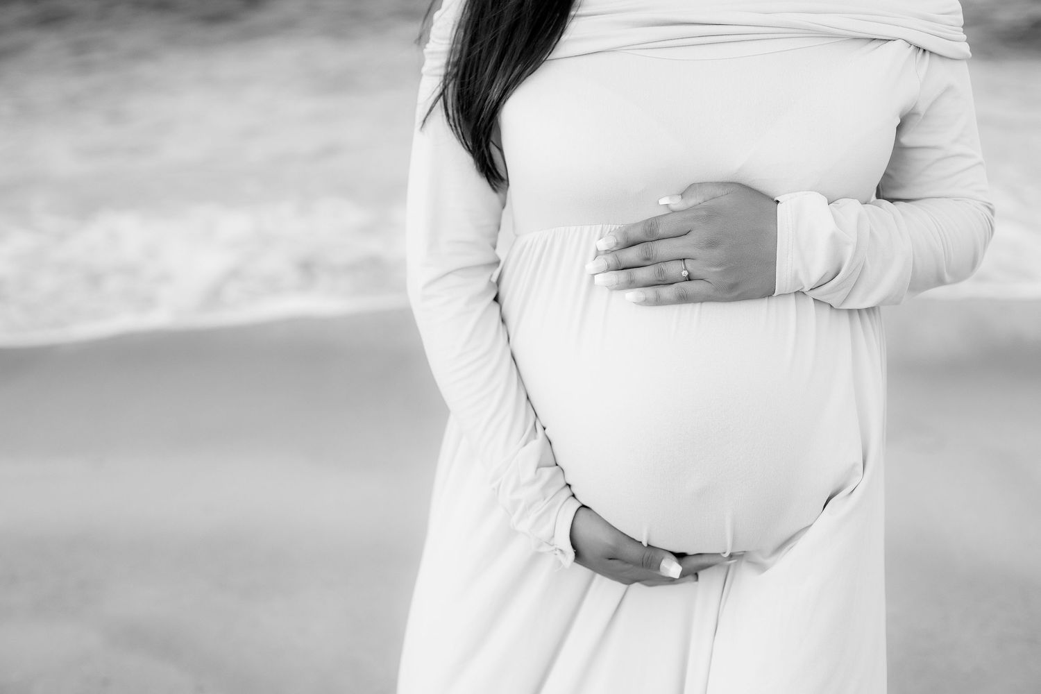 Black and white image of pregnant woman's belly on the best.  Holding above and below her belly.