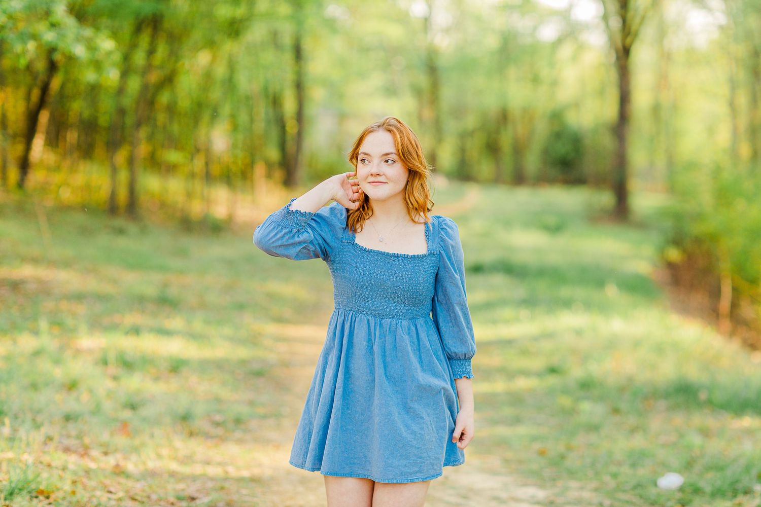 Person in blue dress posing in wooded outdoor setting during golden hour.