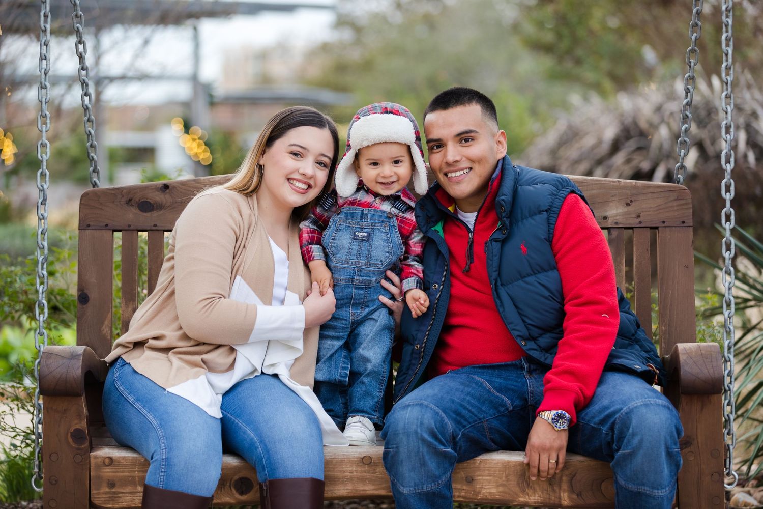 Family sits together on wooden porch swing in casual winter attire.
