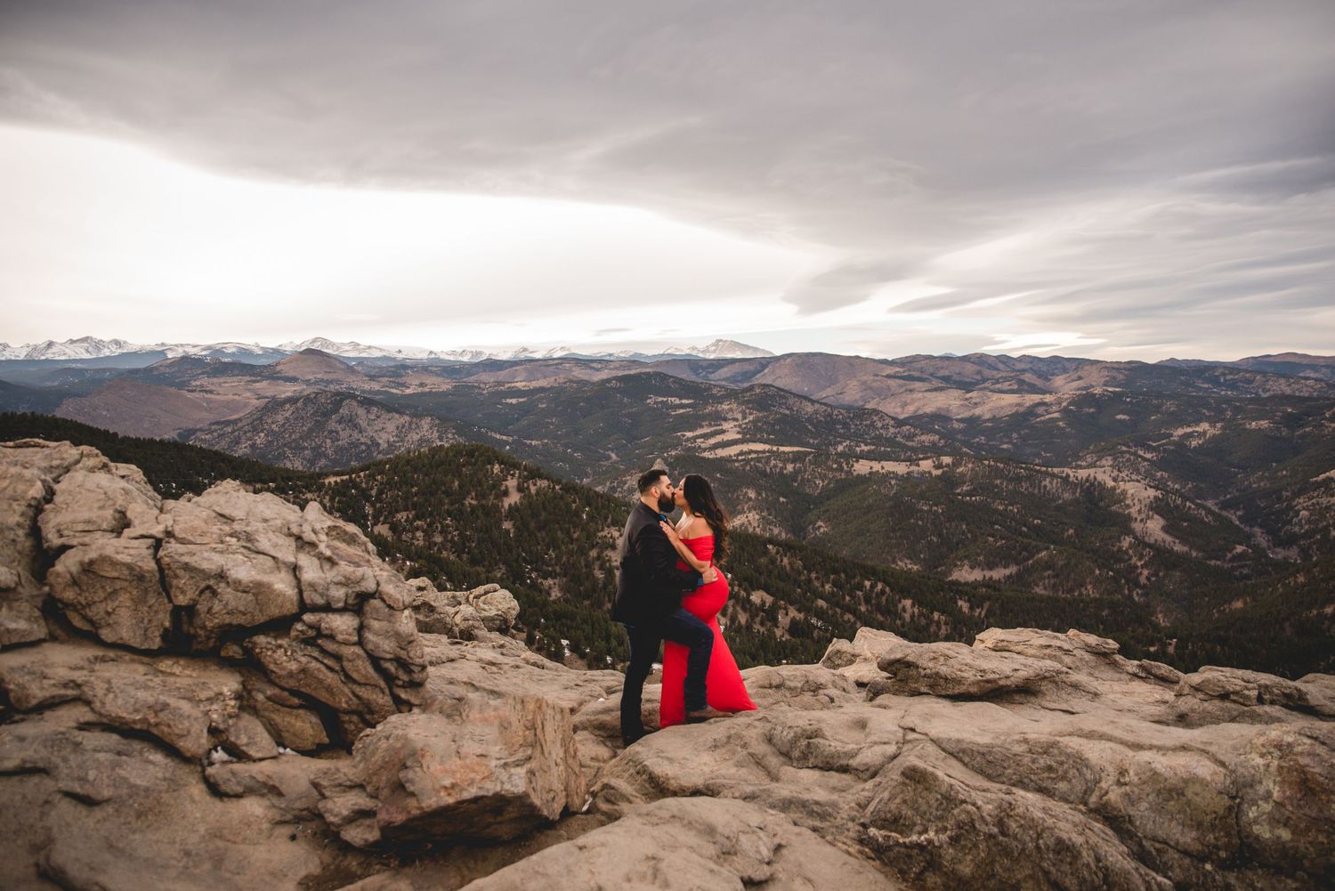 Couple embracing on mountain overlook with expansive valley views.