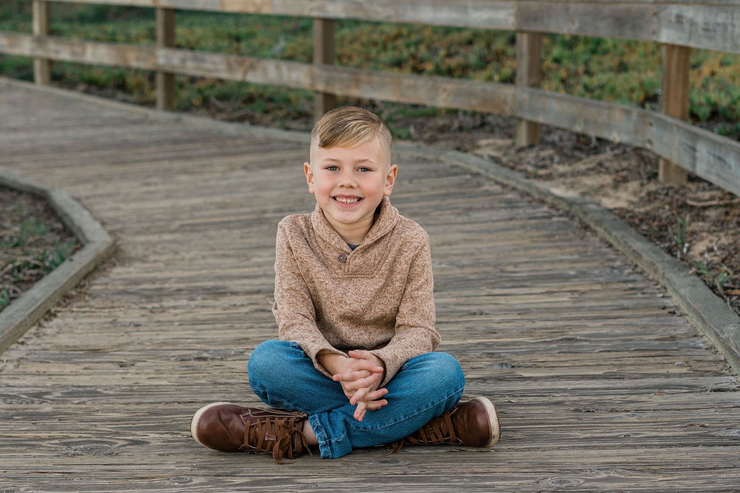 fall family photo session on boardwalk at Pismo Beach with boy in tan sweater, brown boots