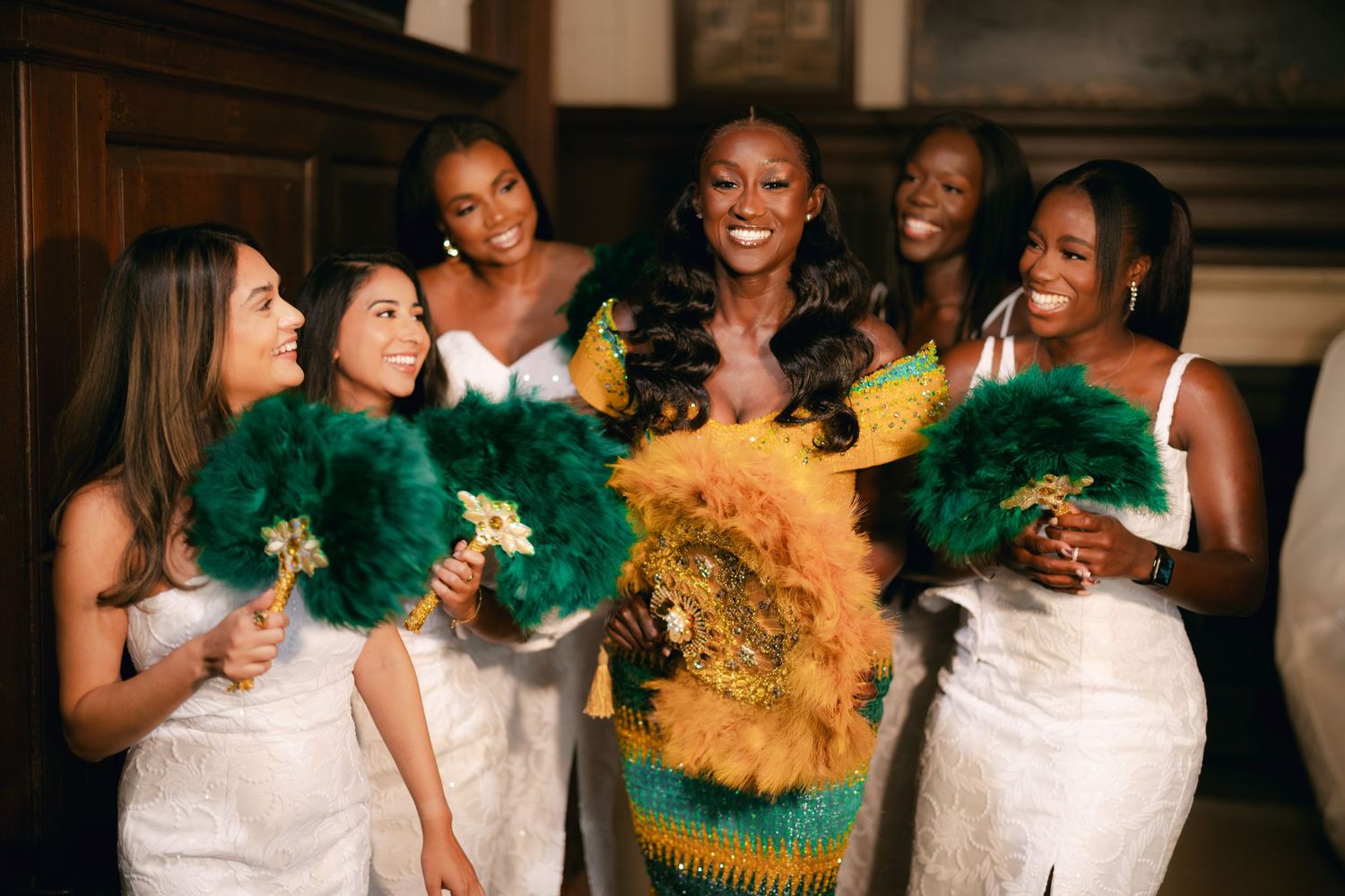 Bridesmaids in white dresses holding vibrant green and gold pom poms celebrate joyfully.