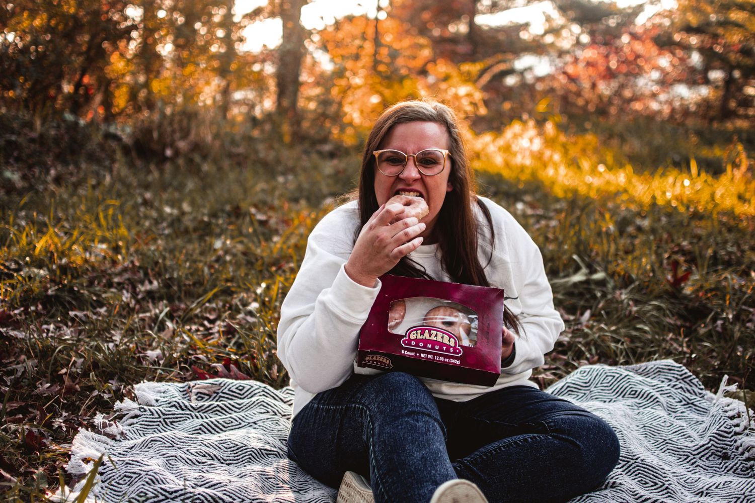 Person enjoying a relaxing autumn picnic on a blanket in the woods at sunset.