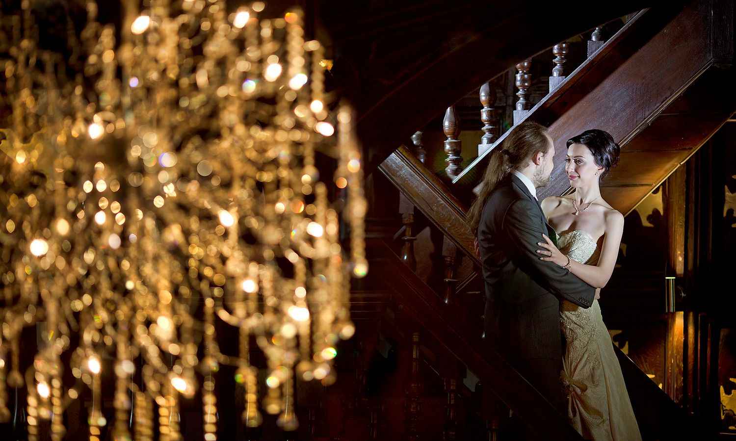 Glamorous wedding couple dancing under ornate crystal chandelier.
